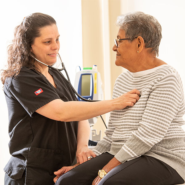 An MA checks the heartbeat of an elderly female patient in the clinic